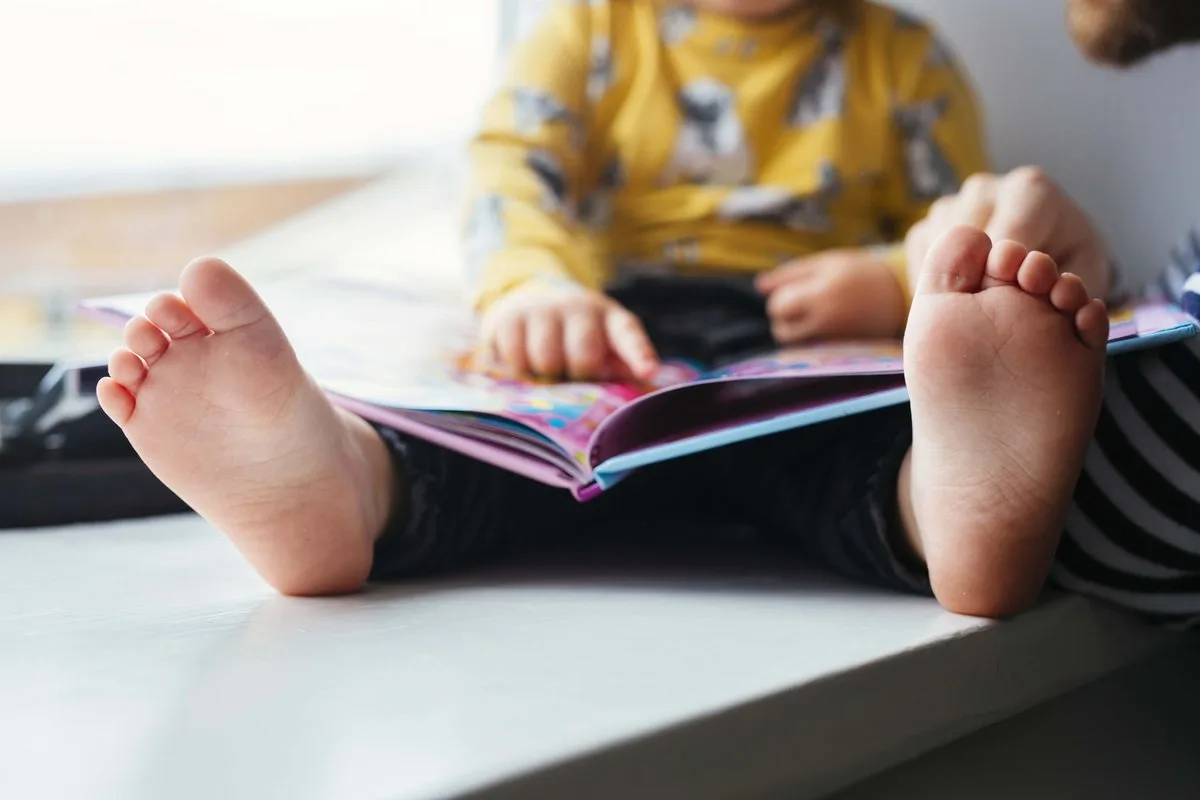 A child sits barefoot on a window sill