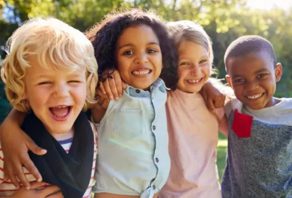 Smiling children hugging outdoors.