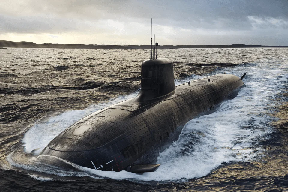 A large black submarine travels on the surface of the sea under a cloudy sky